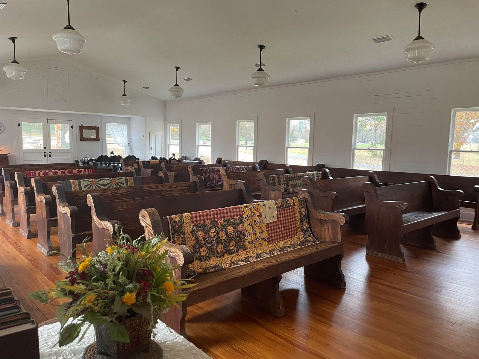 Handmade quilts draped over the chapel pews with wildflowers on the front table