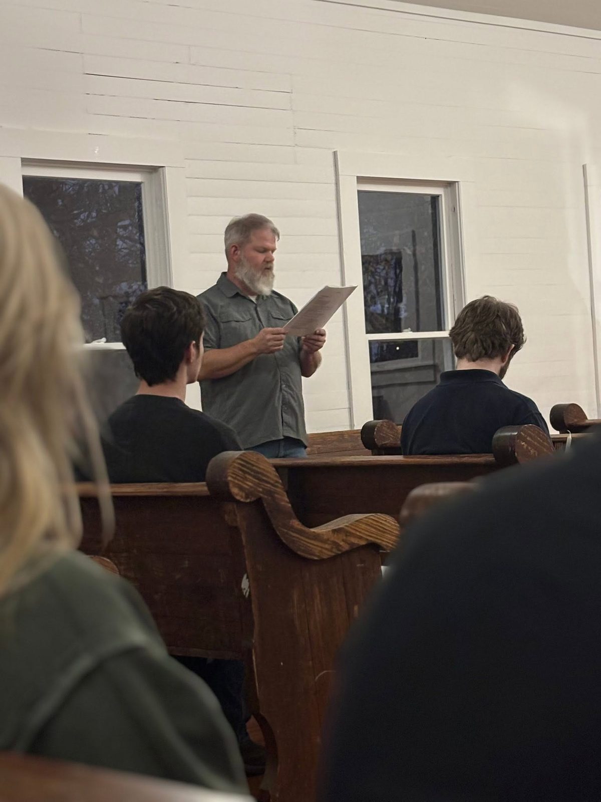 Reading the passage aloud at the front of the chapel while young people follow along from the pews