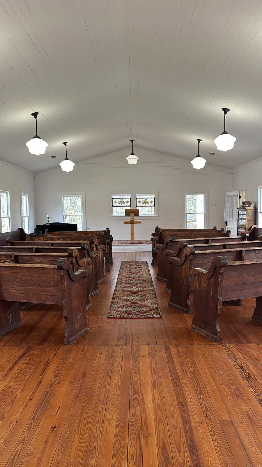The wooden cross and pulpit at the front of the chapel beneath the schoolhouse lights